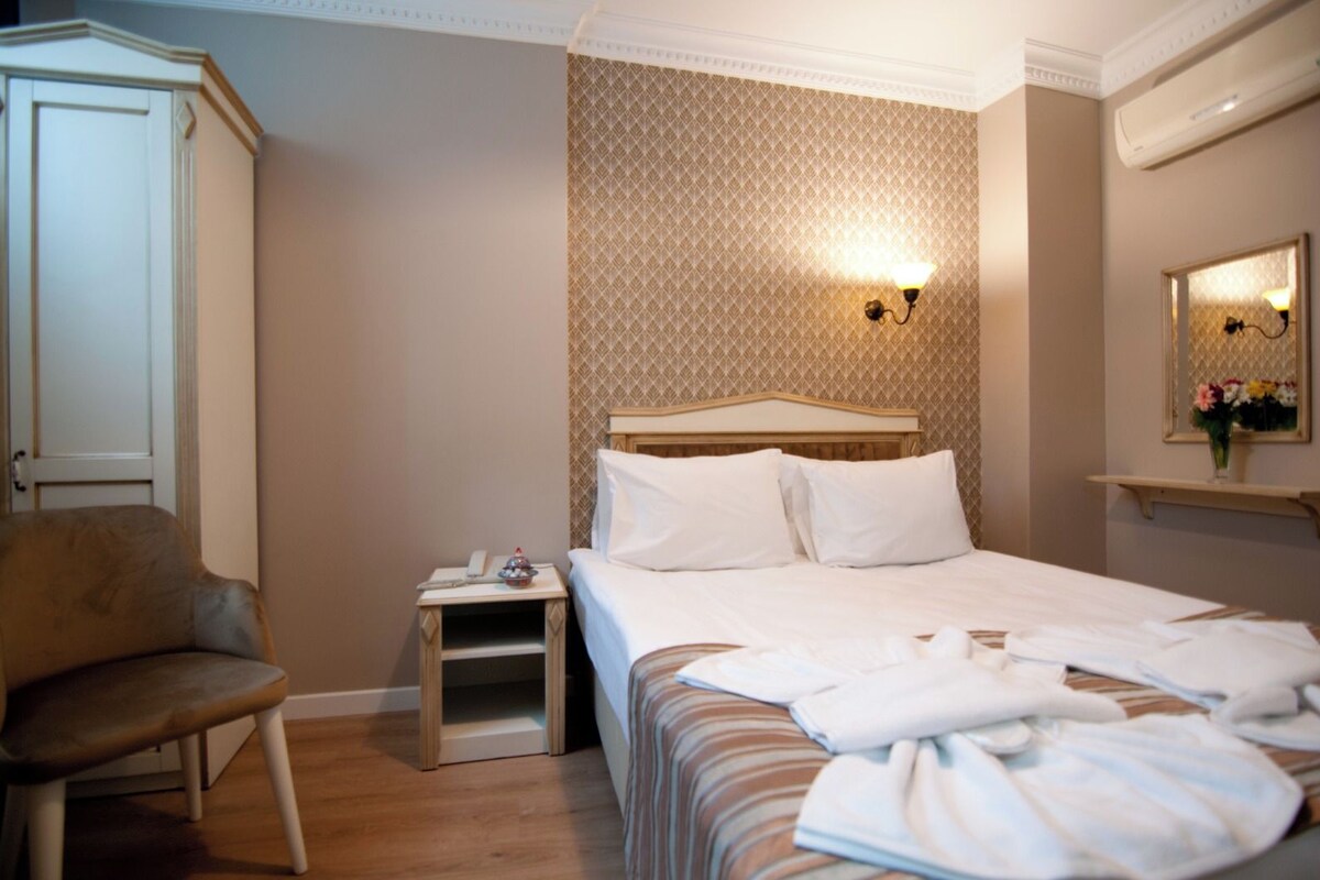 A hotel room with a bed, a nightstand, a chair, a wardrobe, and a wall-mounted mirror.