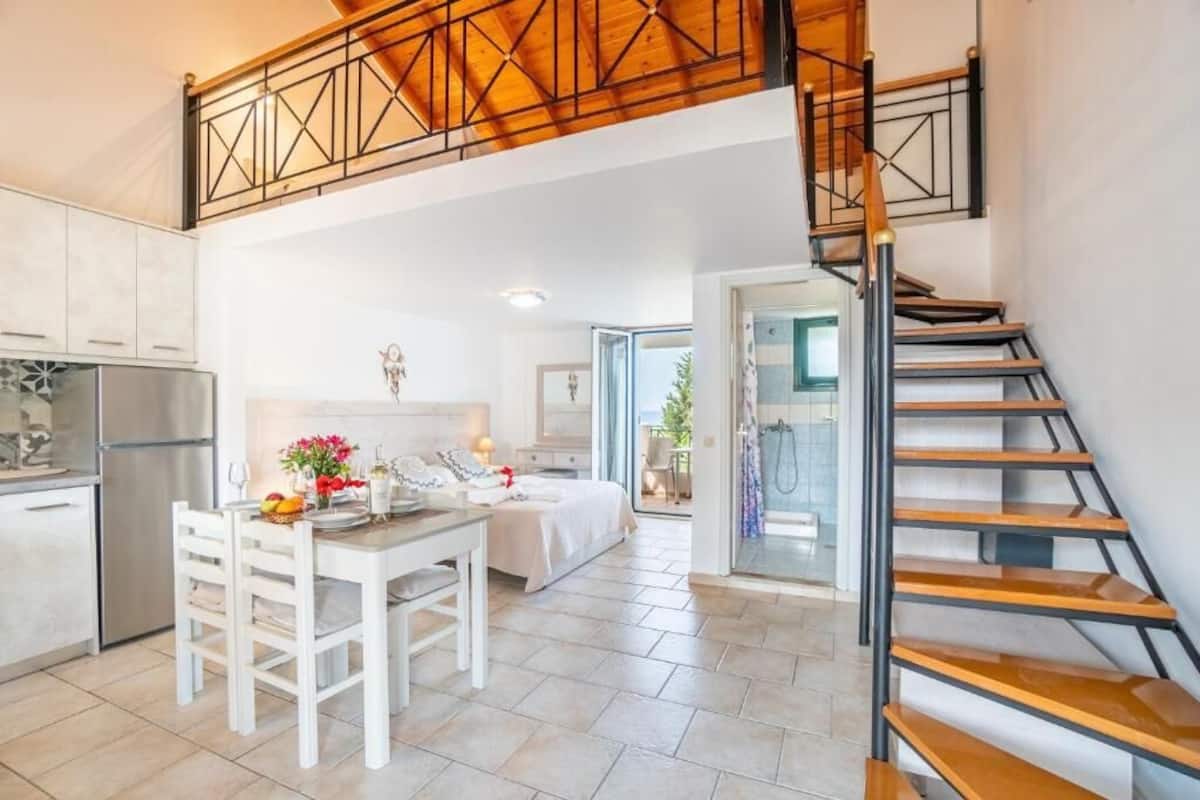 Una cocina moderna con armarios blancos, un comedor con mesa para dos personas y una escalera que lleva a un nivel superior.