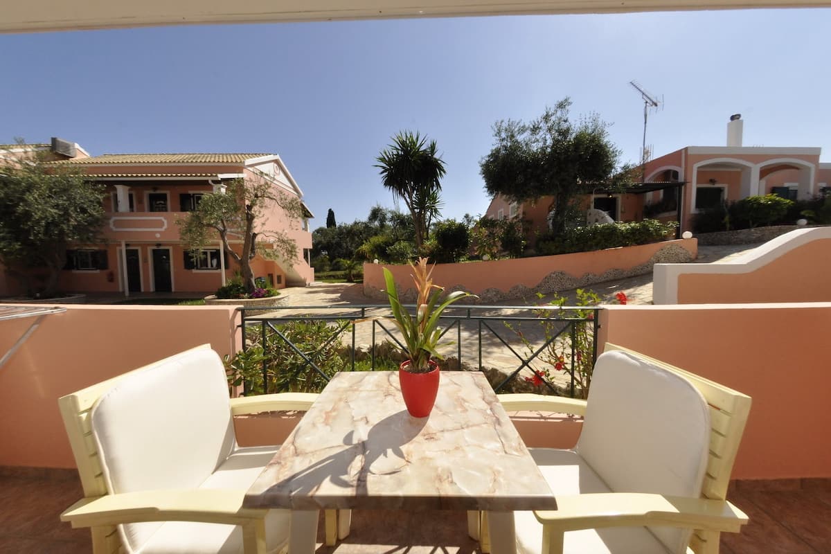 Una terraza con una mesa de mármol y sillas blancas, rodeada por un muro bajo y una palmera.