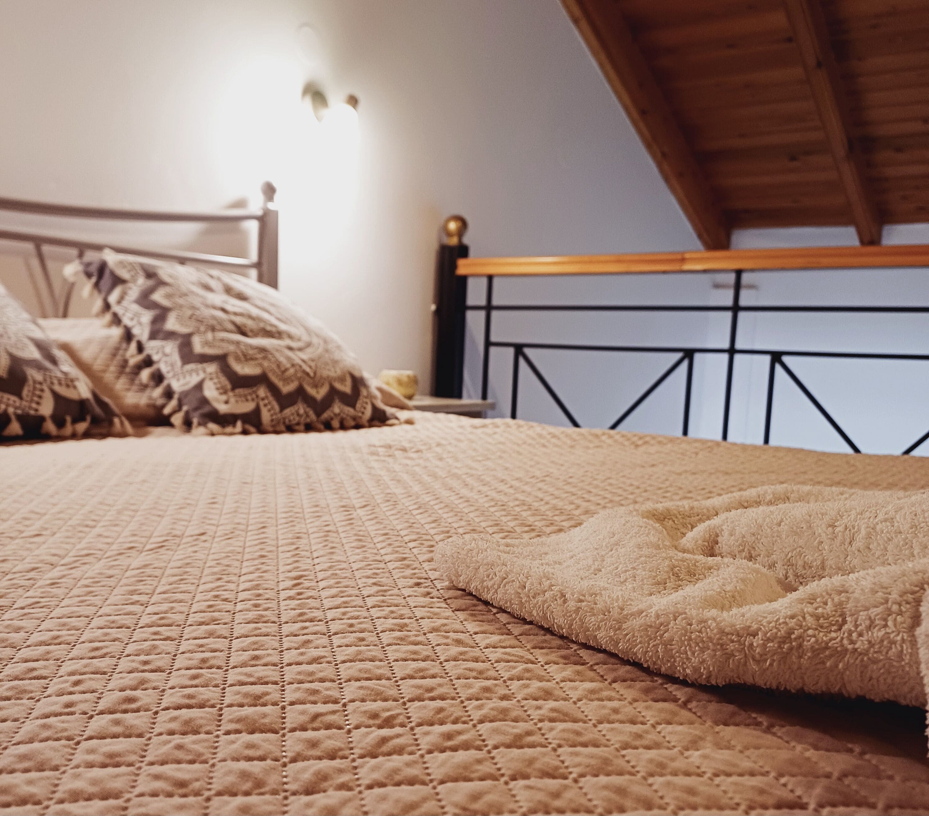 A bed with a quilted cover and a fluffy blanket, a wooden headboard, and a wall-mounted light fixture.