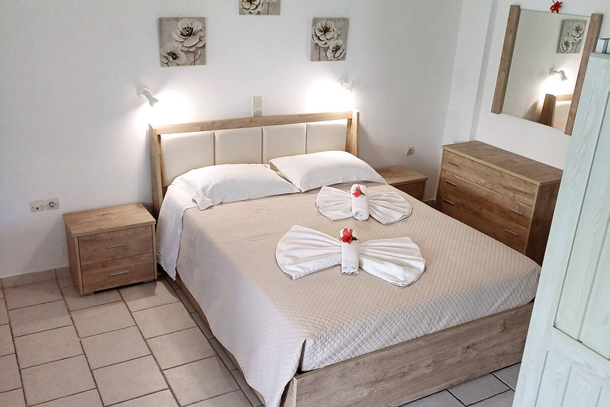 Una cama bien hecha con tablero de madera, una mesita de noche de madera, un aparador de madera y un espejo en la pared.