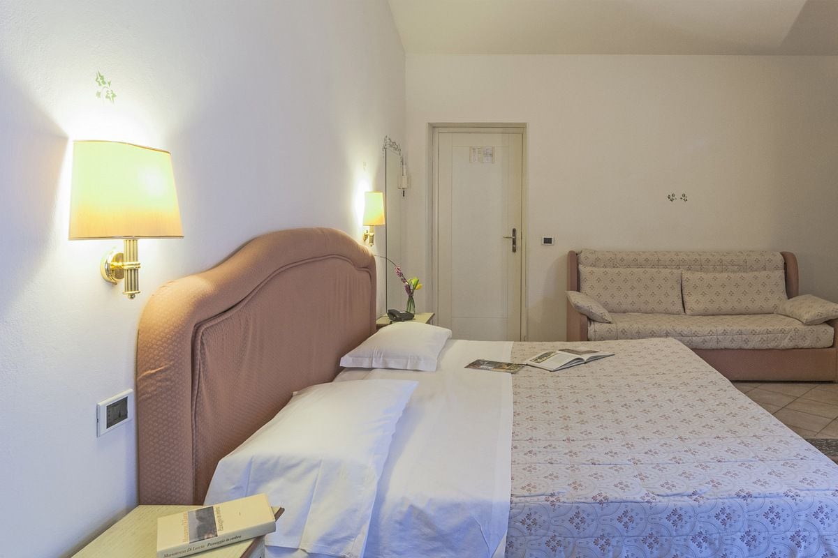 Ein Hotelzimmer mit Bett, Nachttischlampe, Nachttisch, Sofa und einer Tür.