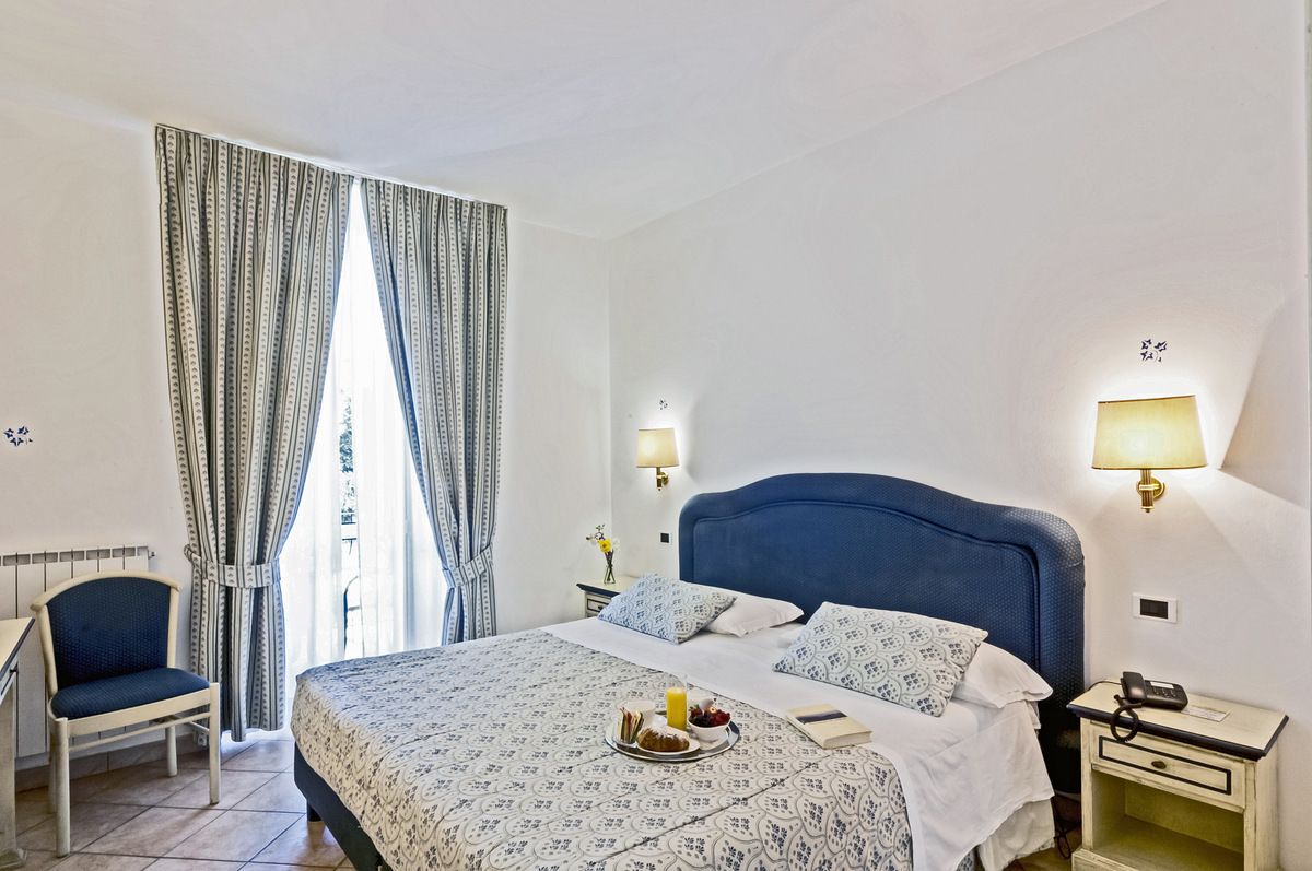 Une chambre d’hôtel avec un lit, une chaise, une table de chevet avec une lampe et des rideaux.