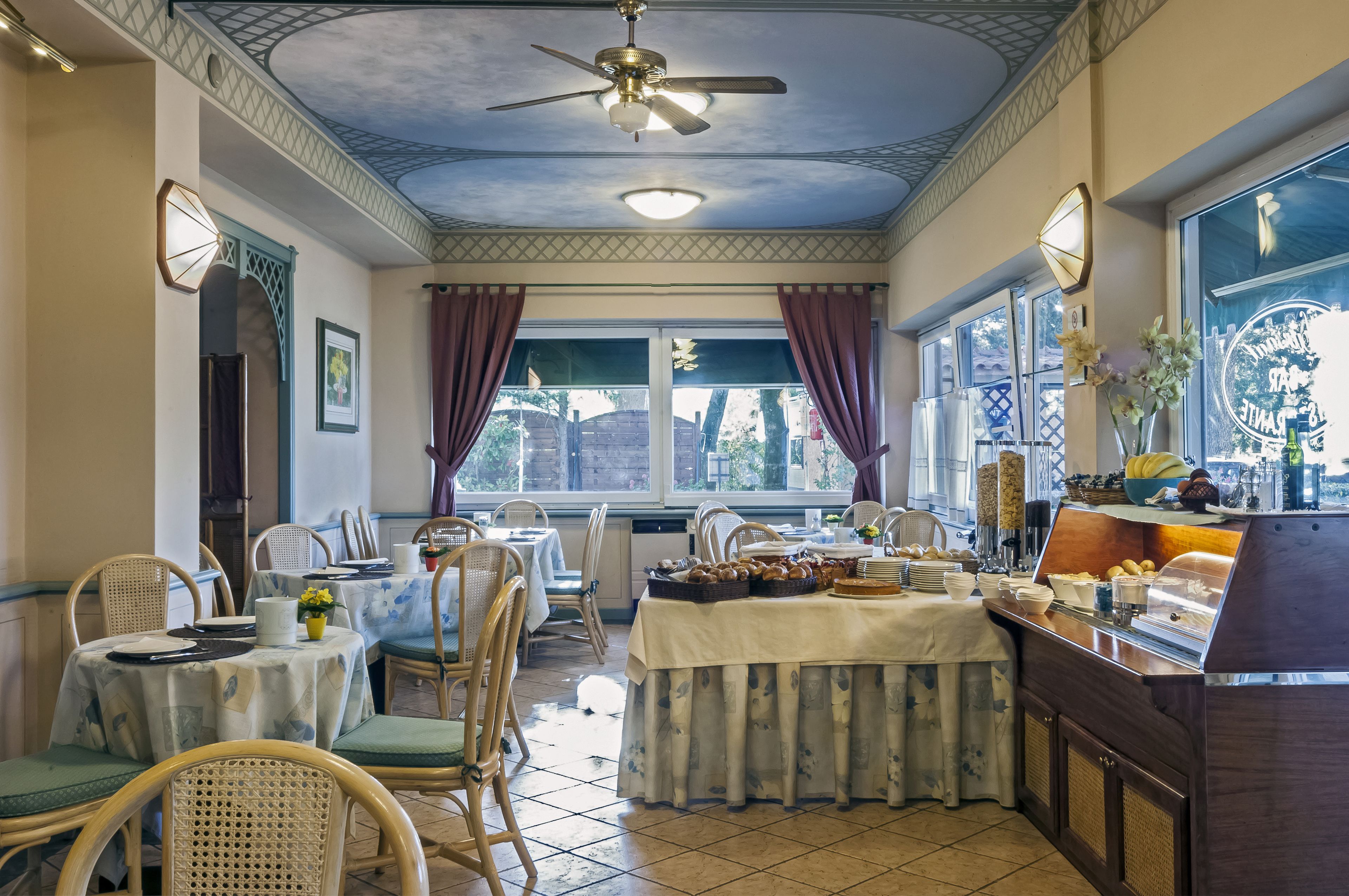 Comedor con mesas dispuestas para el desayuno, una barra de buffet y un ventilador de techo.