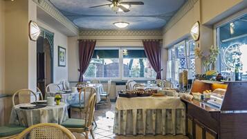 Comedor con mesas dispuestas para el desayuno, una barra de buffet y un ventilador de techo.