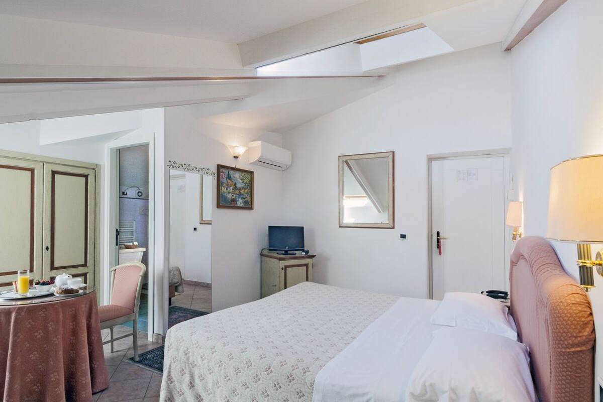 A hotel room with a bed, a desk with a chair, a television, and a dining table with breakfast items.