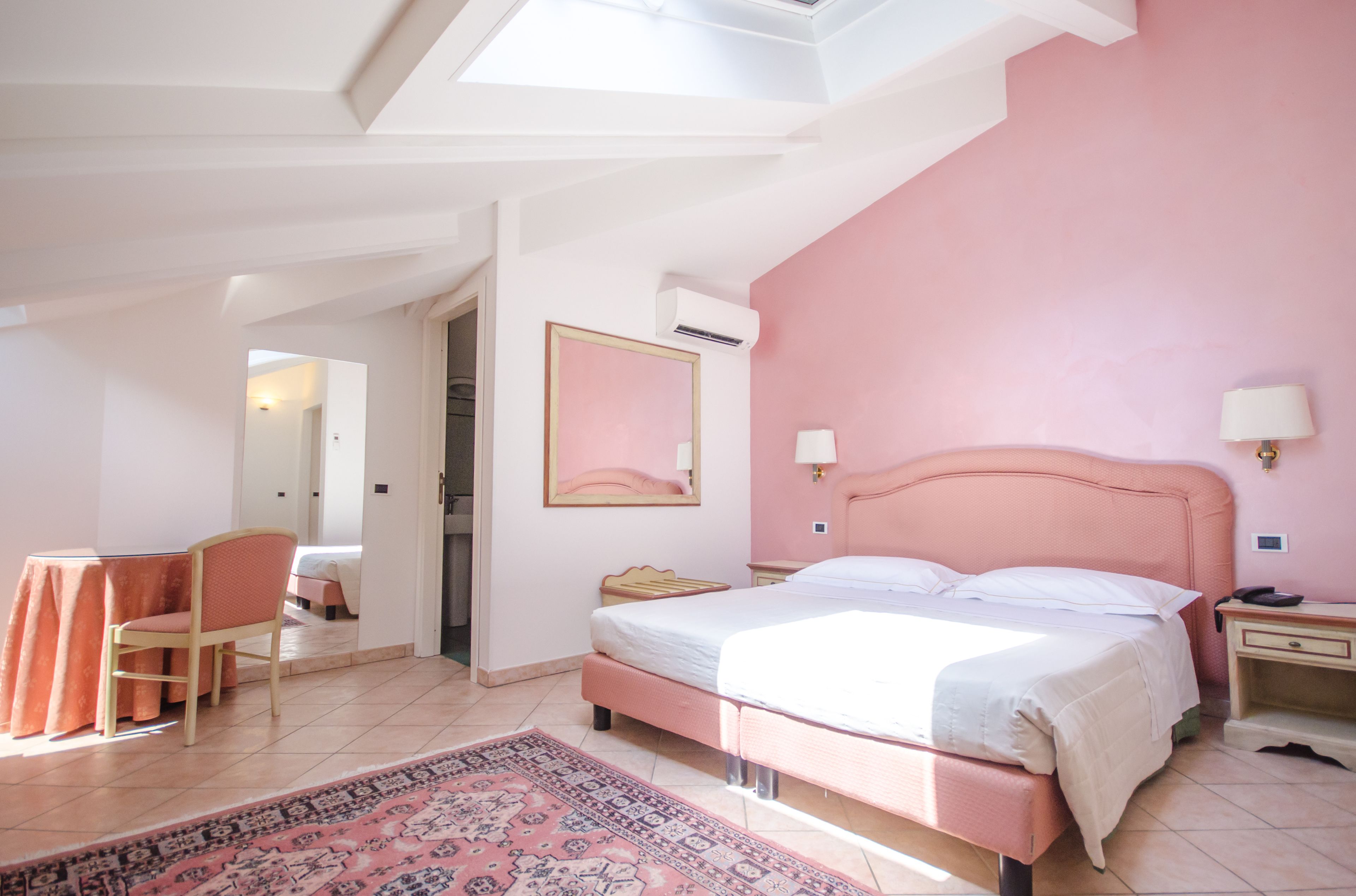Un dormitorio con pared rosa, una cama, un escritorio y una silla.