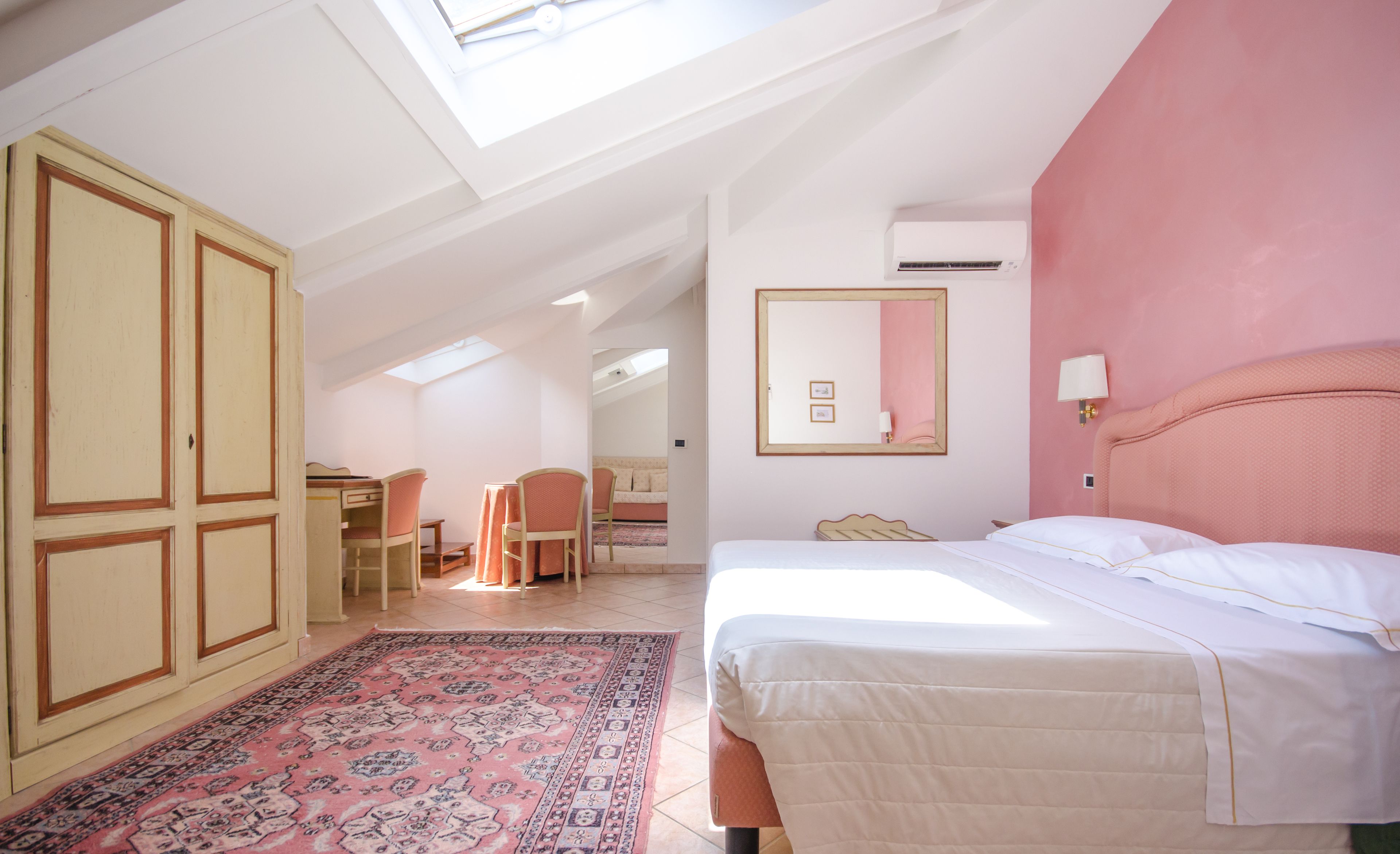 A bedroom with a bed, a desk, a chair, a wardrobe, a mirror, and a skylight.