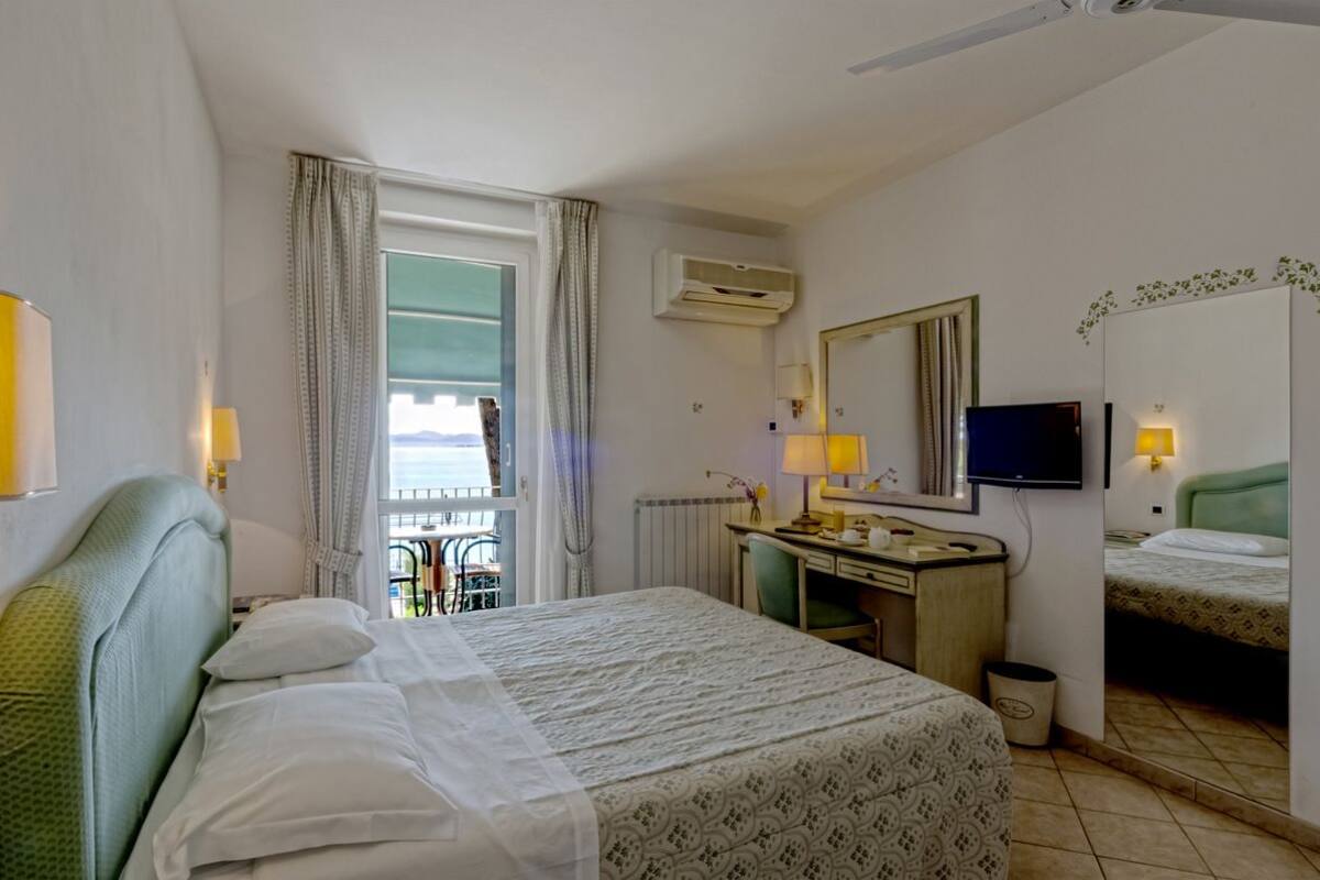 A hotel room with a bed, a desk, a chair, a TV, and a window with curtains.