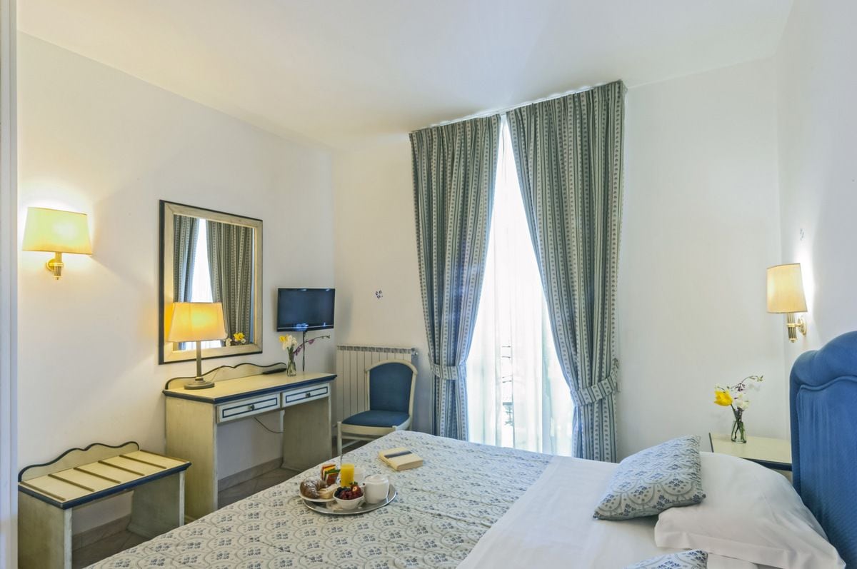 Une chambre d’hôtel comprenant un lit, une table de chevet, un bureau, une chaise et une grande fenêtre avec des rideaux.