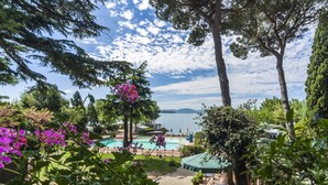 Zona de piscina con vistas a un lago y montañas, rodeada de árboles y plantas en macetas.