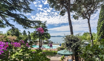 A pool area with a view of a lake and mountains, surrounded by trees and potted plants.