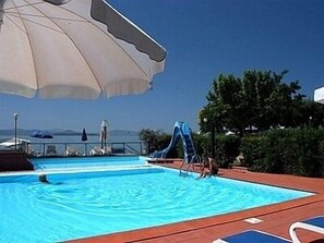 Una piscina con tobogán de agua, sombrillas y vista al mar.