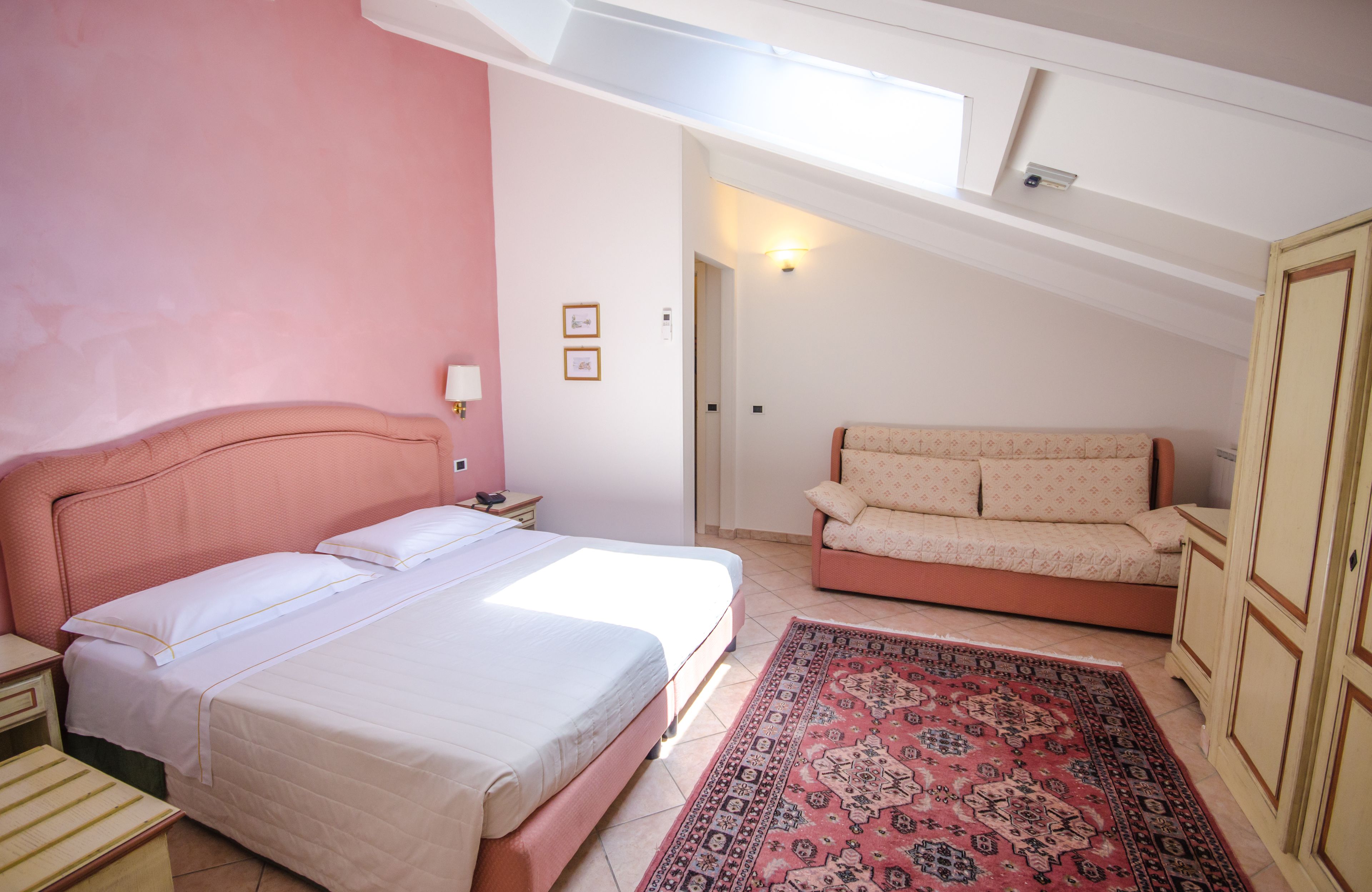 A bedroom with a bed, a sofa, a nightstand, a lamp, and a patterned rug.