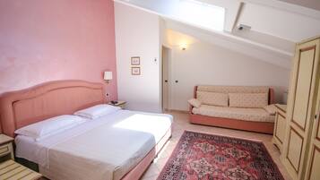 A bedroom with a bed, a sofa, a nightstand, a lamp, and a patterned rug.
