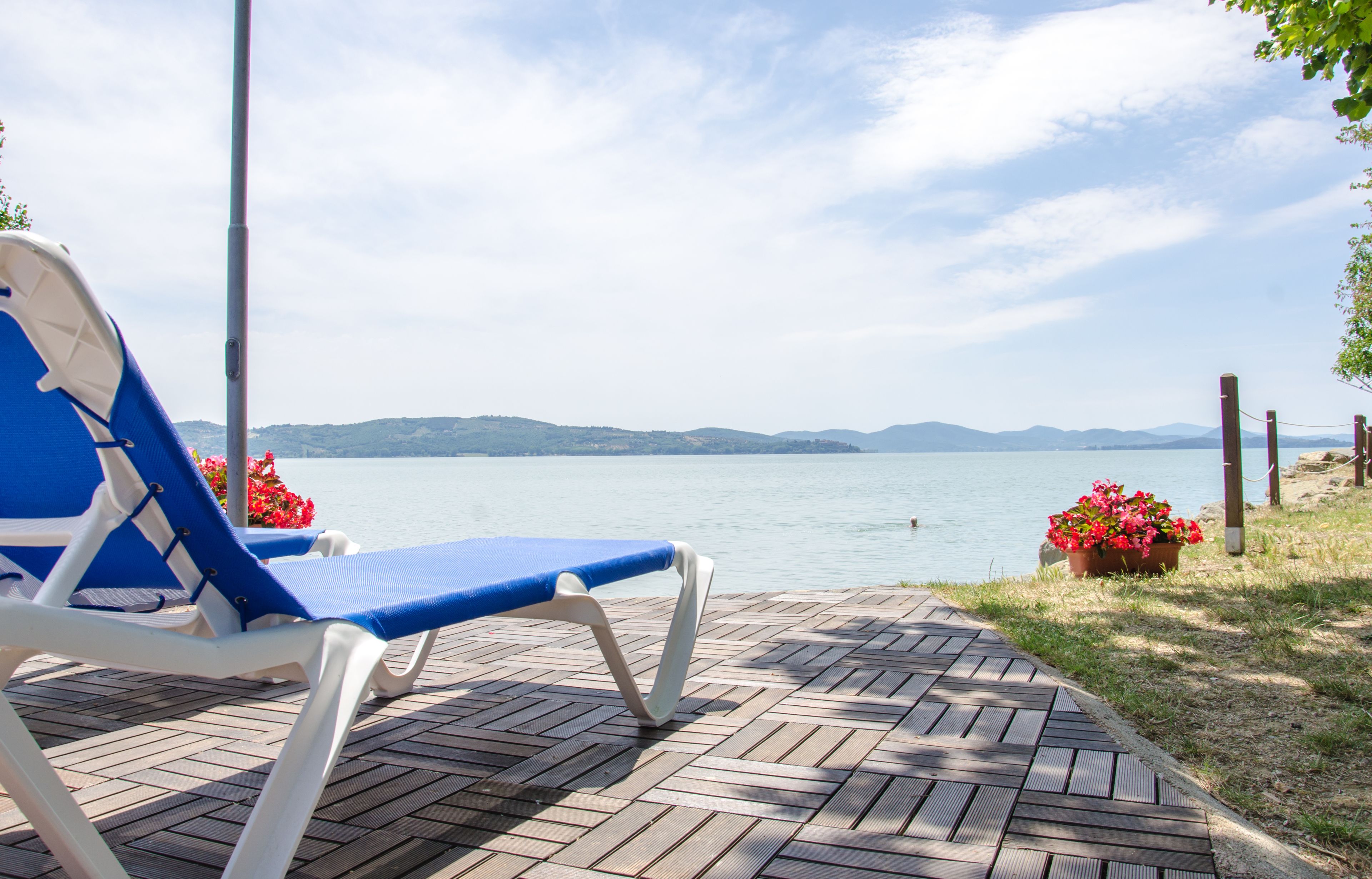 Eine Holzterrasse mit zwei blauen Liegestühlen und einem Blumentopf.