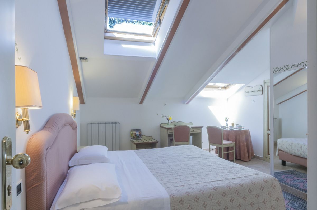 Une chambre à coucher avec un lit, un bureau et une chaise. Il y a une lucarne au-dessus du lit.