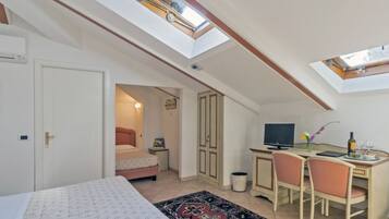 Quarto com claraboia, uma cama, secretária com computador e pequena área de refeições.