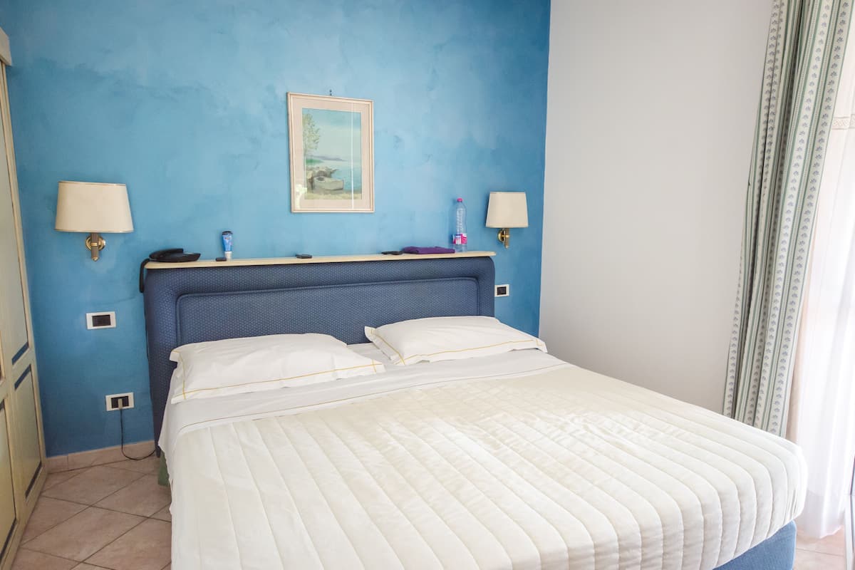 A neatly made bed with a blue headboard, two bedside lamps, and a framed picture on the wall.