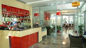 A modern bar area with a red counter, shelves of liquor bottles, and a glass display case. - Hotel Firenze (San Michele al Tagliamento)