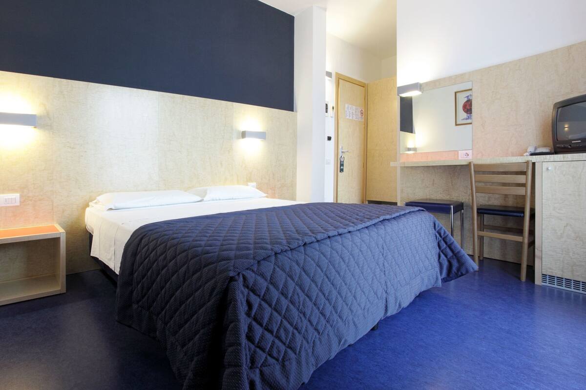 Une chambre d’hôtel comprenant un lit, des tables de chevet, un bureau avec une chaise, une télévision et une armoire.