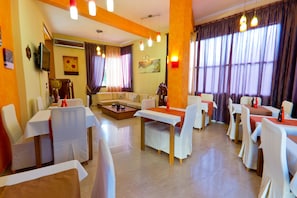 A hotel dining area with tables and chairs, a sofa, and a television.