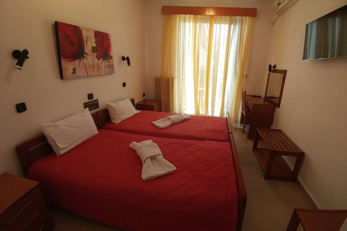 A hotel room with two beds, a TV, a painting, and a window with curtains.