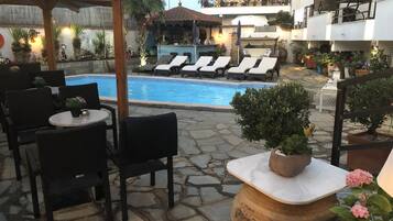 Un área junto a la piscina con sillones de descanso, un bar y un patio con baldosas de piedra.