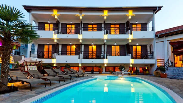 A multi-story hotel with a swimming pool, sun loungers, and a well-lit balcony area.