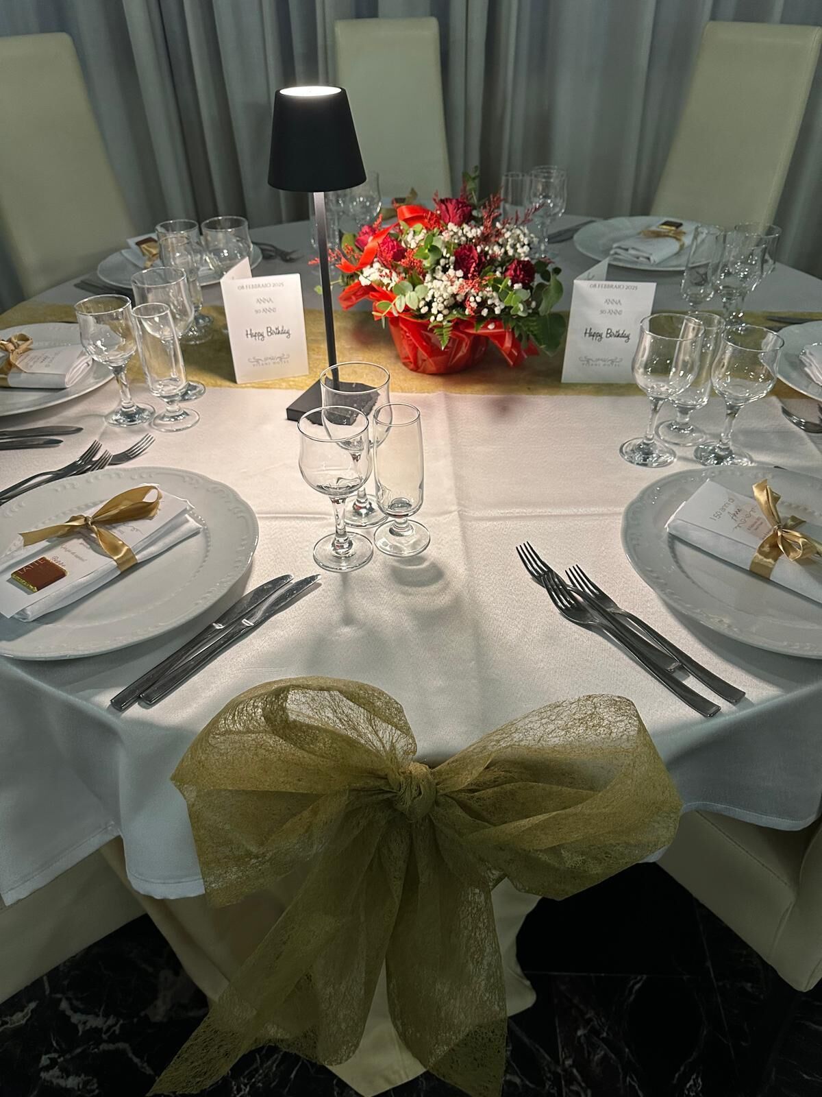 A table set for a formal event with white tablecloths, gold sashes, and clear glassware.