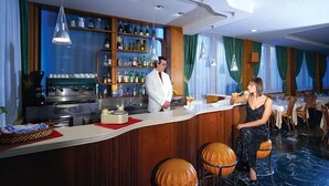 Una zona de bar con un cantinero, una mujer sentada en una mesa y una barra con botellas y vasos.