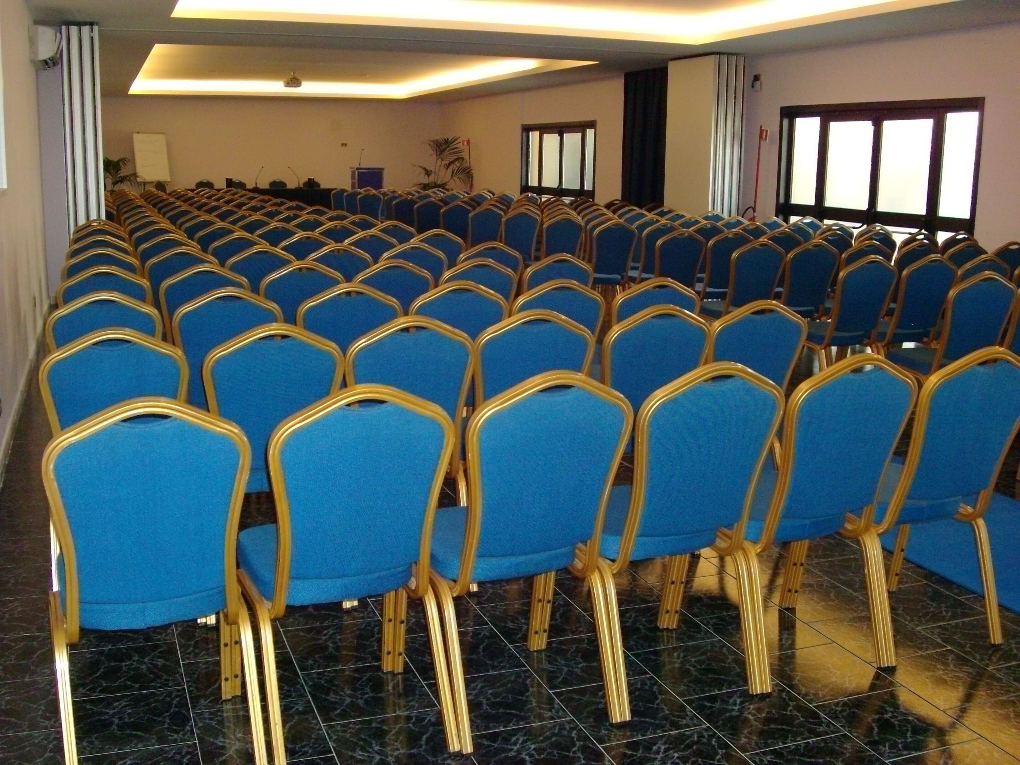 Une salle de conférence avec des rangées de chaises bleues et un pupitre à l’avant.