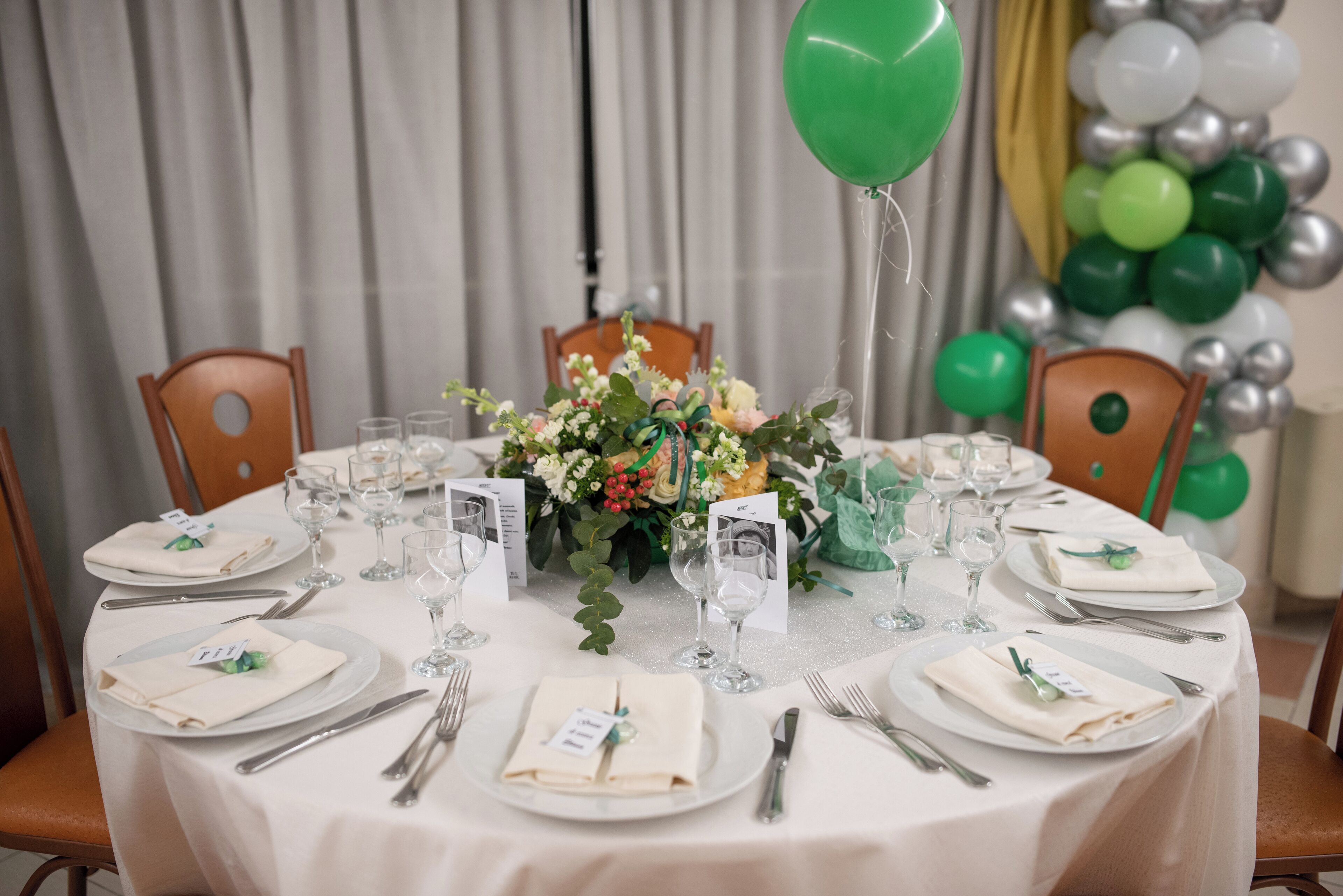 Een gedekte tafel voor een formeel evenement, met witte tafelkleden, borden, bestek en een bloemstuk als decoratie.