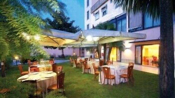 Un espacio de comedor al aire libre con mesas, sillas, sombrillas y un edificio al fondo.