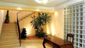Una escalera conduce a una plataforma con una mesa y sillas de madera, una planta en maceta y una alfombra estampada sobre un piso de baldosas.