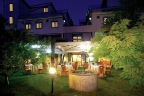 An outdoor dining area with tables and chairs, a wooden barrel, and a covered seating area. - Pisani Hotel (San Nicola La Strada)
