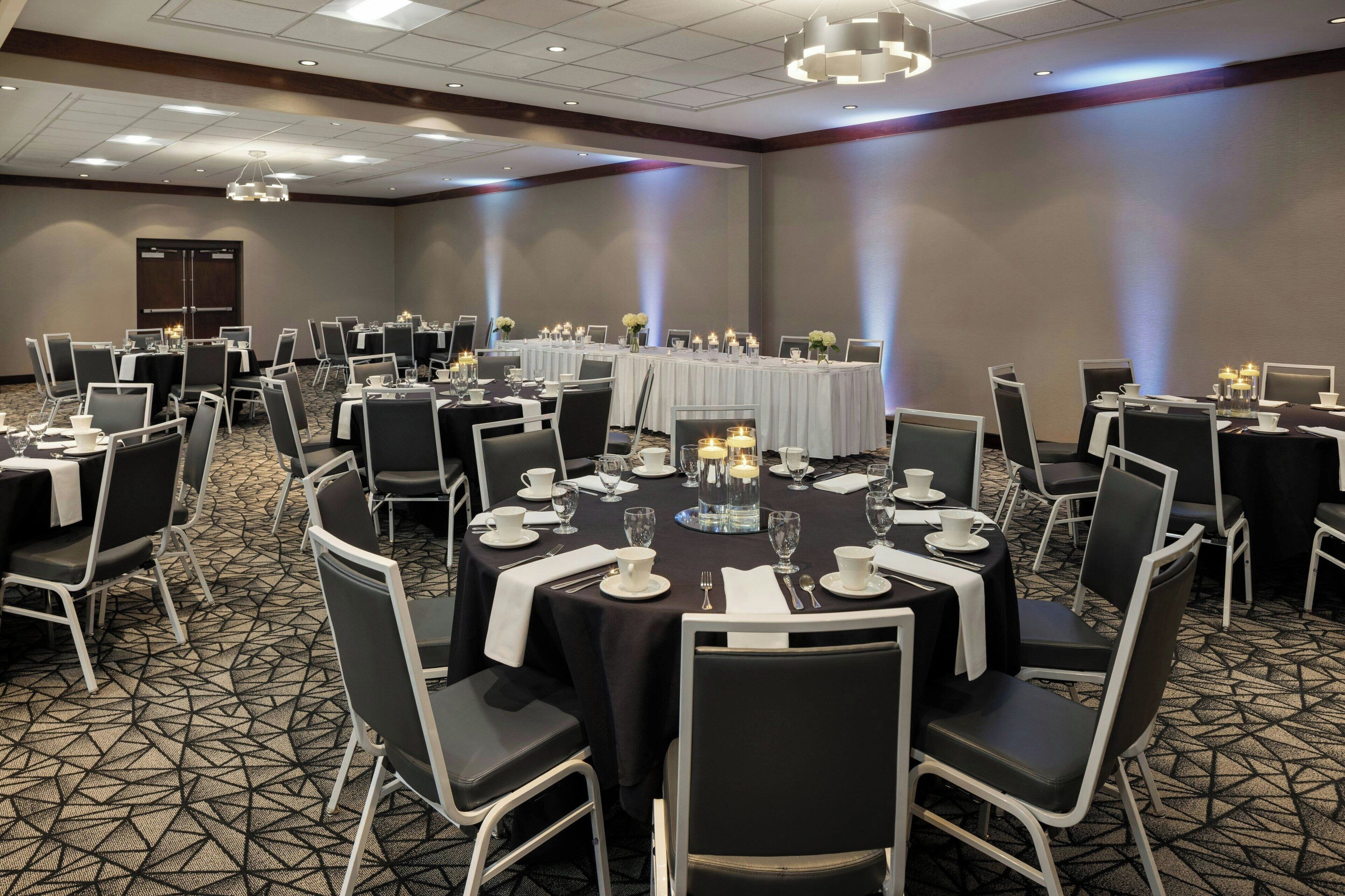 Une salle de conférence avec des tables rondes, des chaises noires et des nappes blanches.