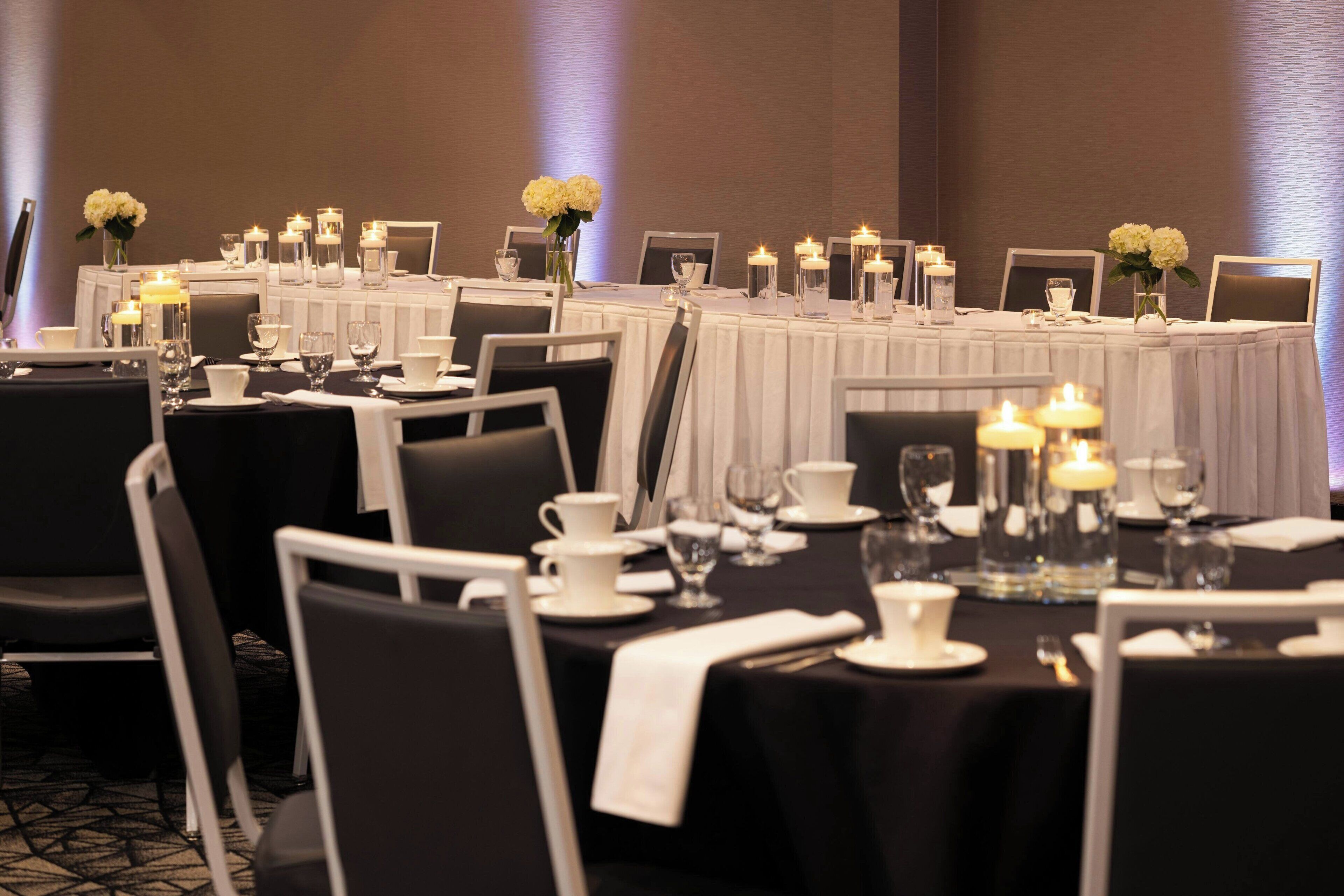 Un salón de banquetes con mesas dispuestas para un evento formal, con manteles blancos, velas y centros de mesa florales.