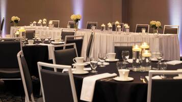 Un salón de banquetes con mesas dispuestas para un evento formal, con manteles blancos, velas y centros de mesa florales.