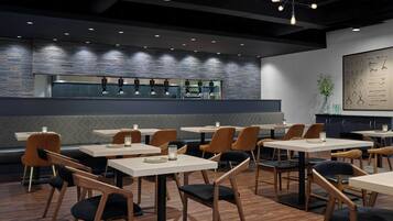 Un interior de restaurante moderno con mesas y sillas de madera, una pared de acento de ladrillo e iluminación colgante.