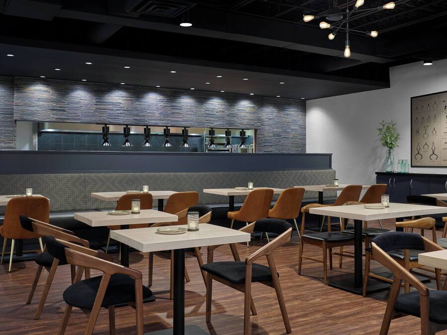 Un interior de restaurante moderno con mesas y sillas de madera, una pared de acento de ladrillo e iluminación colgante.
