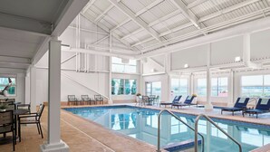 Una piscina interior con vistas a la ciudad, rodeada de sillones y mesas.