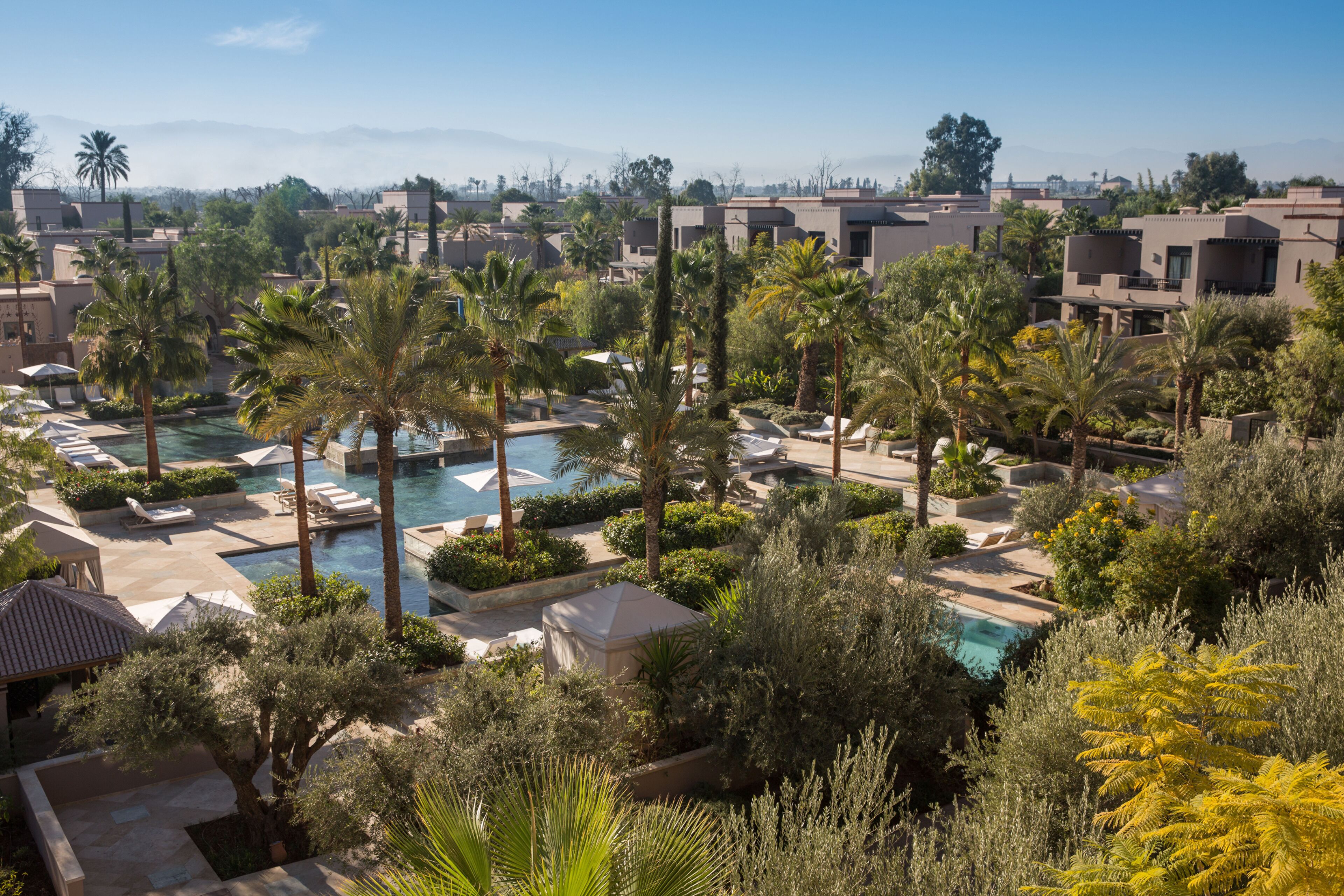 Ein Resort mit mehreren Swimmingpools, umgeben von Palmen und Liegestühlen.