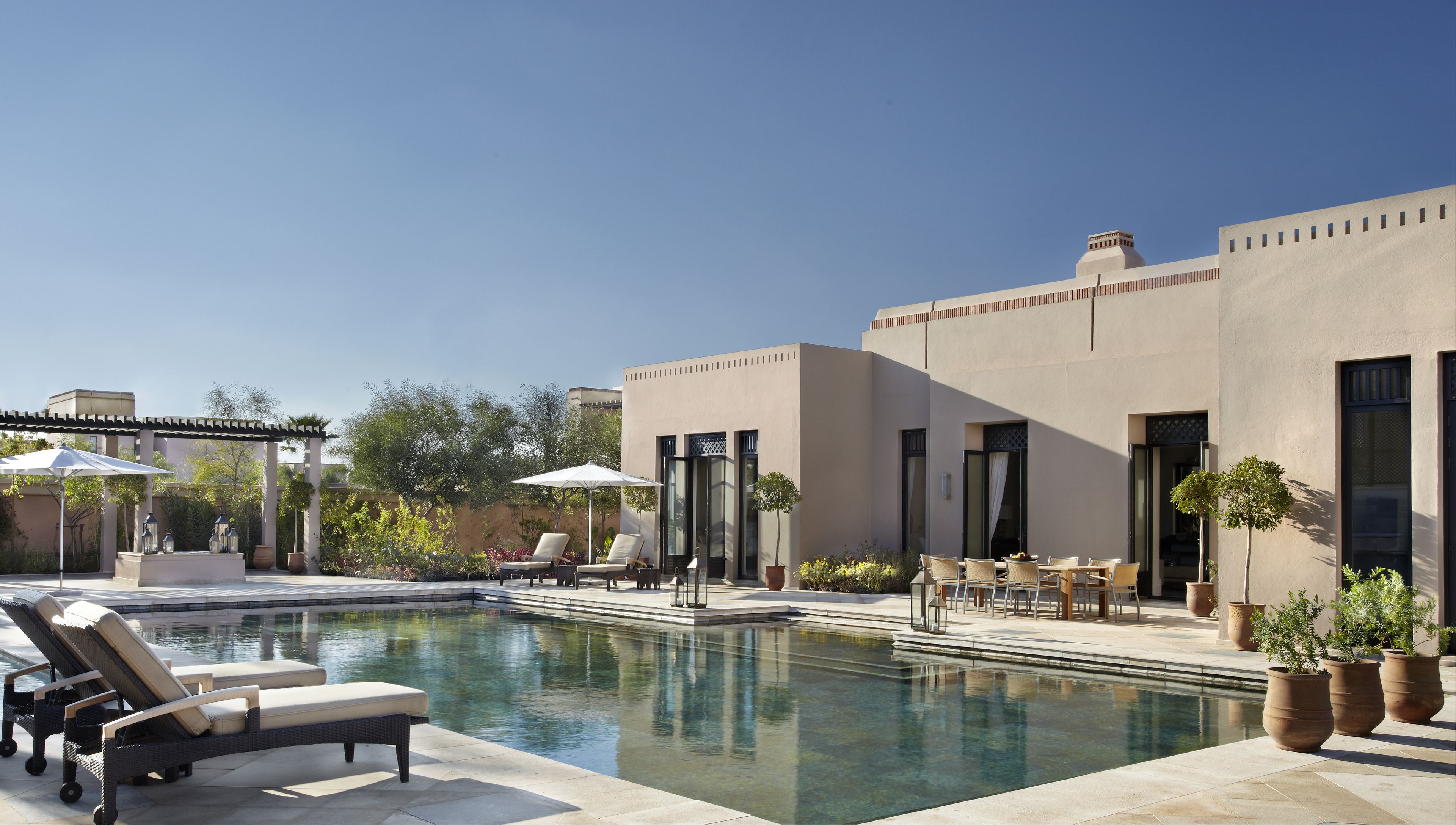 A pool area with lounge chairs, umbrellas, and potted plants.