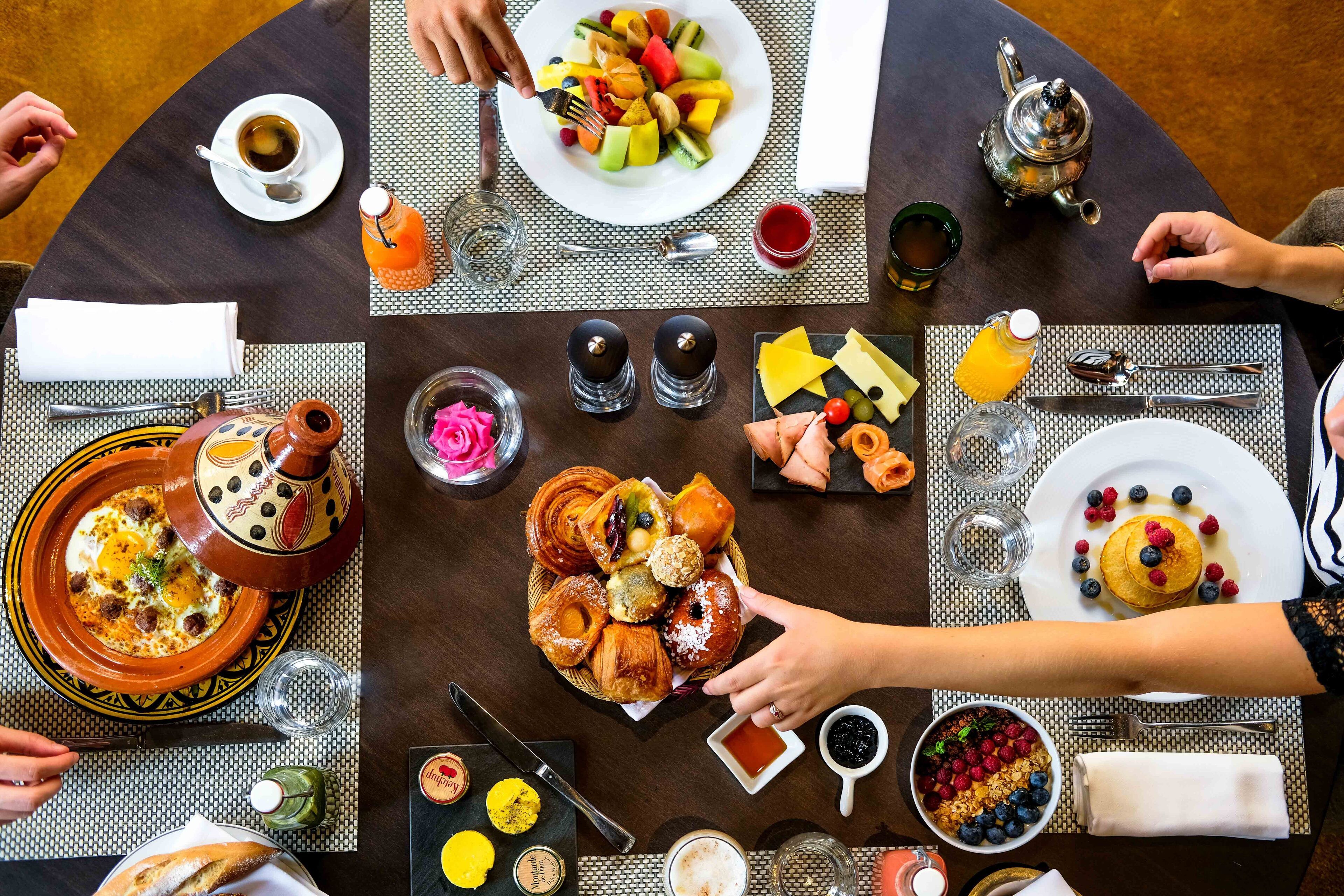 A round dining table with various breakfast items, including pastries, fruits, and beverages.