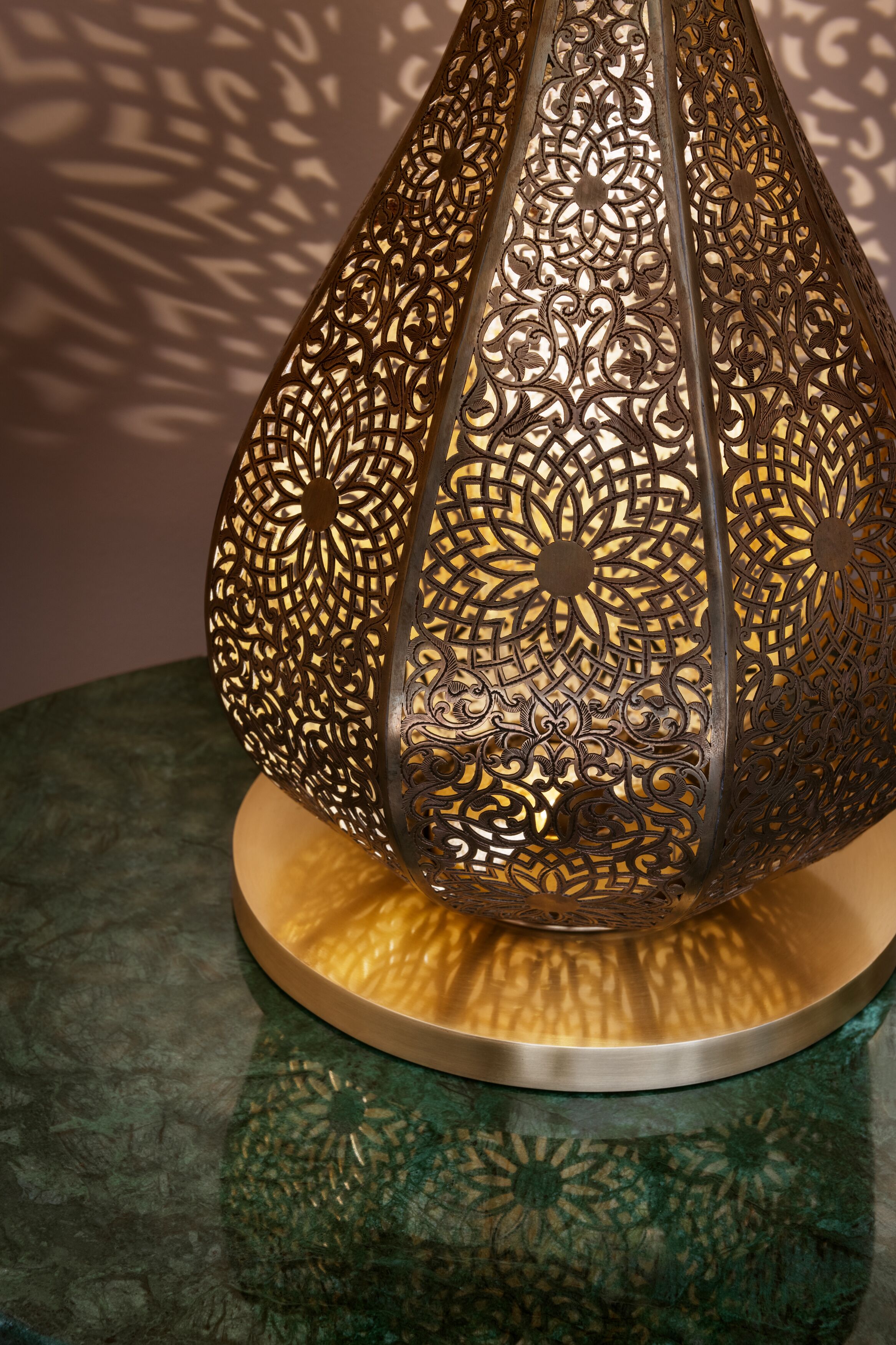 A decorative metal lantern with intricate patterns, placed on a round, textured base.