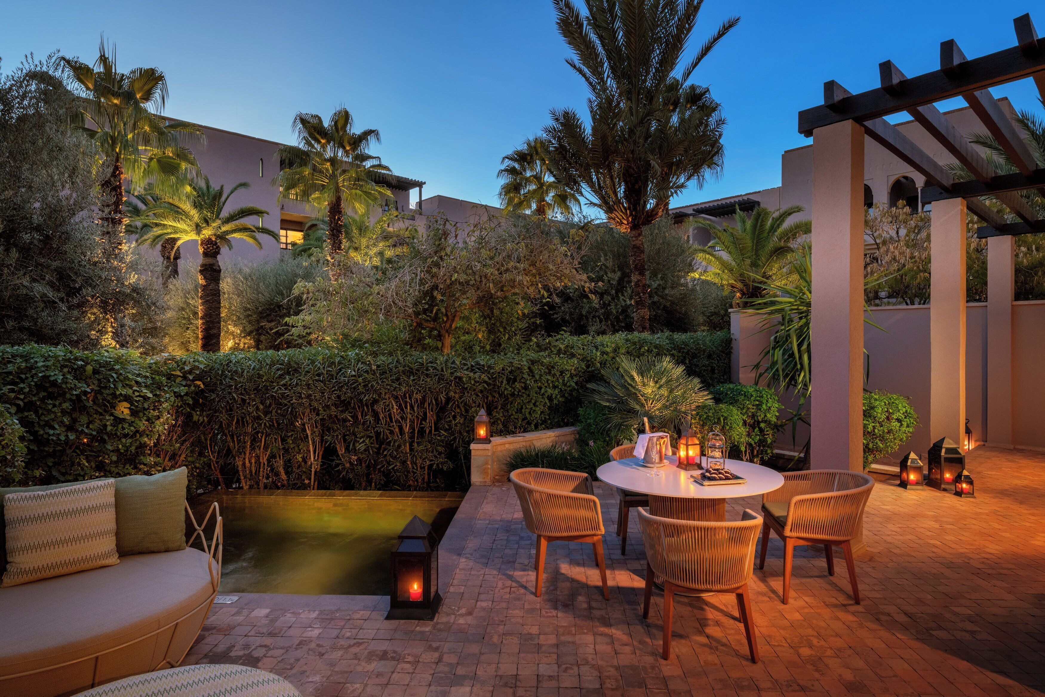 An outdoor patio with a round table and chairs, a cushioned seating area, and a small water feature.