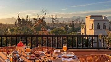 A dining table set with breakfast items, a glass of orange juice, and a view of mountains and trees.