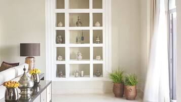 Una habitación con un aparador blanco con puertas de vidrio que exhibe varios objetos decorativos, un sofá con cojines, una lámpara y dos plantas en macetas.