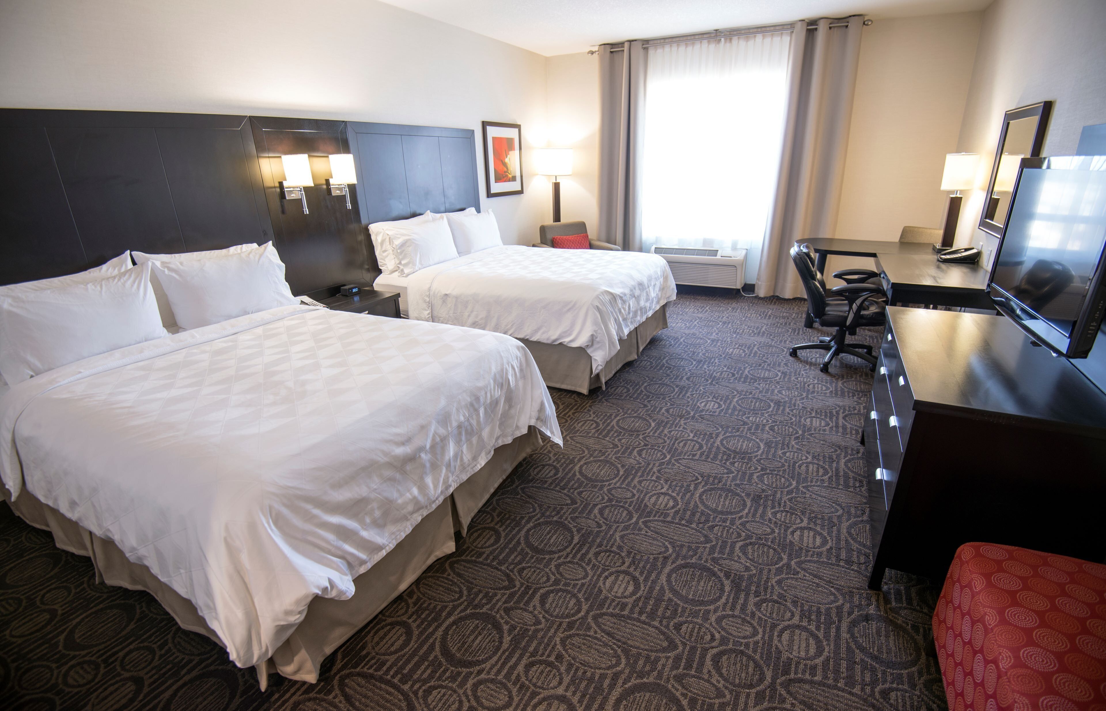 A hotel room with two beds, a desk, a chair, and a television.